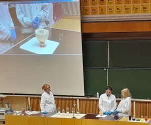 Prowadzący pokazy z uczennicą prezentują spieniony płyn w pucharku na ekranie