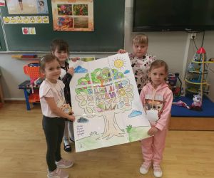 Czworo dzieci z oddziału przedszkolnego prezentuje wspólny plakat w kształcie drzewa z kolorowymi liśćmi i napisem „Razem silni jak drzewo”.