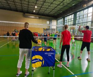 Troje trenerów odbija piłki do uczniów za siatką