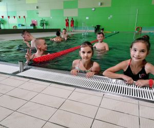 Uczniowie w strojach kąpielowych pływają w basenie.