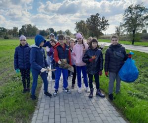 Uczniowie klasy piątej podczas zbierania śmieci przy chodniku prowadzącym do kościoła