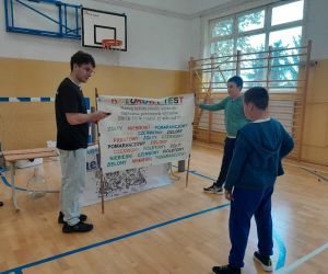 Prowadzący trzyma kolorowy transparent, uczeń stoi przodem do niego