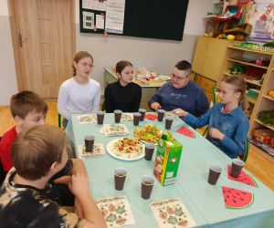 Grupa uczniów przy wspólnym stole, przygotowująca przekąski warzywne.