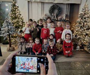 Grupa dzieci pozująca w świątecznej dekoracji z choinkami i zimowymi akcentami.