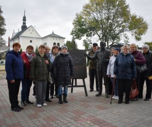 Hrubieszów. Grupa Ludzi w otoczeniu figury Wiktora Zina przy sztaludze, w głębi kościół.