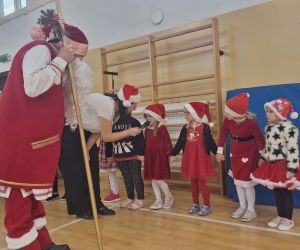 Dzieci stoją przed Mikołajem, czekając na rozdanie prezentów na sali gimnastycznej.
