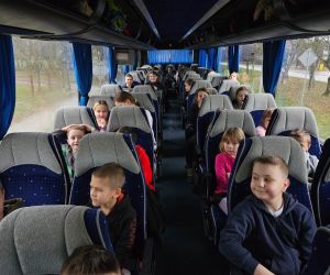 Uczniowie siedzą w autokarze podczas przejazdu; część z nich spogląda w stronę aparatu.