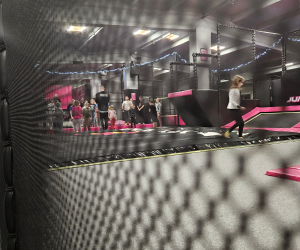 Uczniowie stoją i bawią się w strefie trampolin w parku trampolin; zdjęcie wykonane zza siatki zabezpieczającej.