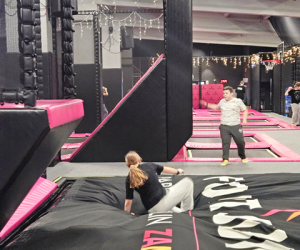 Dwoje uczniów korzysta z poduszki powietrznej i trampolin; w tle widoczne są elementy toru przeszkód i dekoracje świetlne.