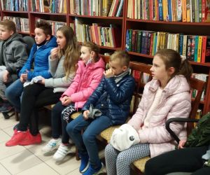 Grupa dzieci w bibliotece. Dzieci siedzą na krzesłach.
