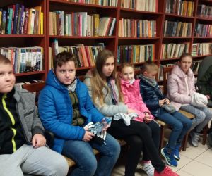 Grupa dzieci w bibliotece. Dzieci siedzą na krzesłach.