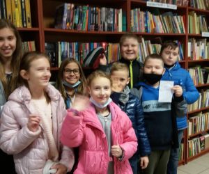 Grupa dzieci w bibliotece, na tle półek z książkami.