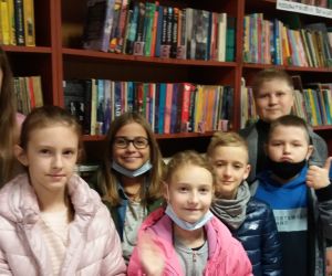 Grupa dzieci w bibliotece, na tle półek z książkami.