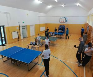 Widok z góry na salę gimnastyczną, gdzie uczniowie rozgrywają mecze tenisa stołowego