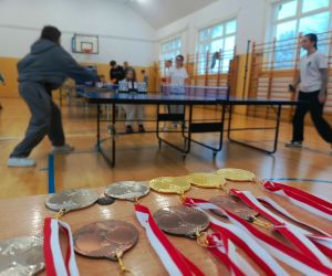 Na pierwszym planie medale dla laureatów turnieju, w tle uczniowie grający w tenisa stołowego