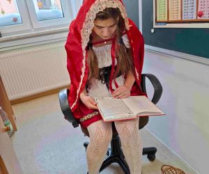 Uczennica klasy siódmej w stroju 
Czerwonego Kapturka czyta baśń młodszym uczniom