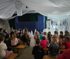 Widok sali podczas spektaklu „Królowa Śniegu”; dzieci obserwujące występ aktorów i kukiełek.