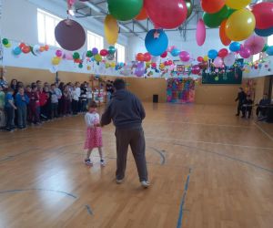 Uczeń prowadzący trzyma mikrofon i wręcza  uczennicy kartkę walentynkową.