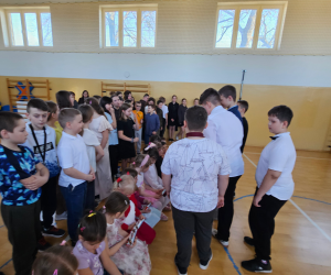 Chłopcy wręczają dziewczynkom słodkie upominki podczas szkolnych obchodów Dnia Kobiet, a pozostali uczniowie stoją wokół i obserwują wydarzenie.