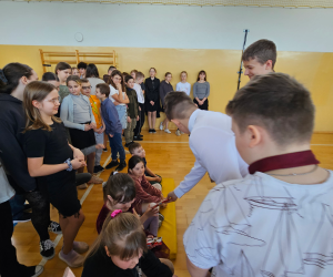 Uczniowie szkoły oraz dzieci z oddziałów przedszkolnych zgromadzeni na sali gimnastycznej podczas szkolnej uroczystości z okazji Dnia Kobiet.