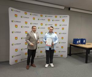 Uczeń prezentuje dyplom i nagrodę po zakończeniu konkursu, stojąc obok przedstawiciela władz gminy.