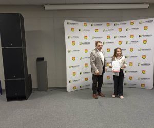 Uczennica prezentuje dyplom i nagrodę po zakończeniu konkursu, stojąc obok przedstawiciela władz gminy.