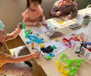 Dzieci przy stoliku wykonują prace plastyczne z wykorzystaniem kolorowej bibuły i materiałów plastycznych.