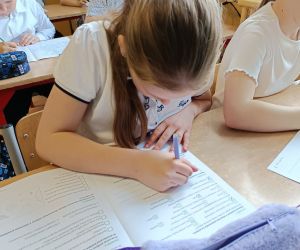 Uczennica pochylona nad kartą pracy zapisuje odpowiedzi na pytania.
