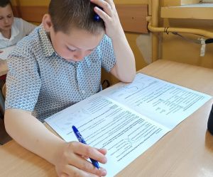 Uczeń siedzi przy ławce, zastanawiając się nad rozwiązaniem zadania w arkuszu.