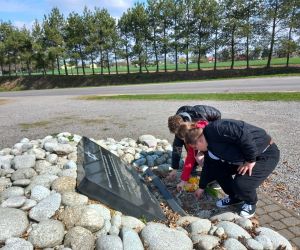 Uczniowie składają bukiet żółtych żonkili przy tablicy pamiątkowej w Cichoborzu, znajdującej się w otoczeniu kamieni.