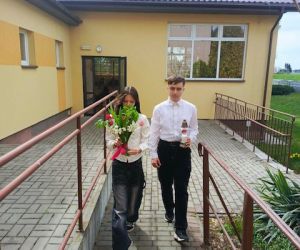 Uczniowie w drodze do tablicy pamiątkowej z kwiatami i zniczem