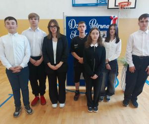 Uczniowie stoją przed dekoracją związaną z Dniem Patrona Szkoły