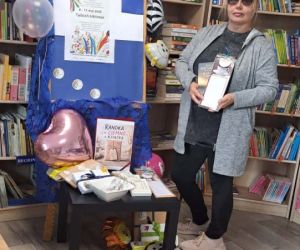 Na zdjęciu widoczna jest kobieta w otoczeniu regałów z książkami przy dekoracjach związanych z świętem bibliotek. 