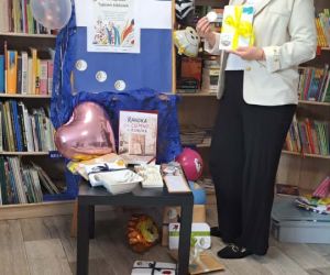 Na zdjęciu widoczna jest kobieta w otoczeniu regałów z książkami przy dekoracjach związanych z świętem bibliotek. 