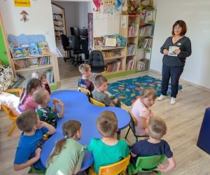 Na zdjęciu widoczna jest grupa dzieci słuchająca podczas lekcji bibliotecznej.