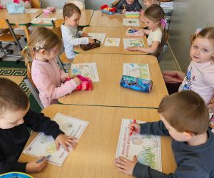 Dzieci kolorują karty pracy o tematyce ekologicznej przy stolikach w sali.