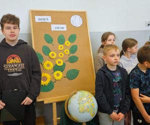 Uczniowie stoją podczas apelu z okazji Dnia Ziemi obok dekoracji i globusa.