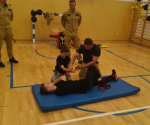 Uczeń układa kolegę w pozycji bezpiecznej pod okiem strażaka