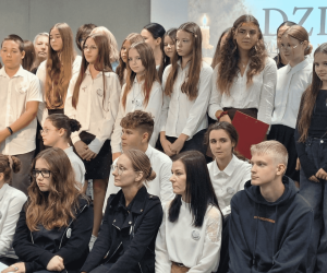Grupa uczestników Narodowego Czytania „Dziadów” Adama Mickiewicza. Uczniowie i dorośli ustawieni są do wspólnej fotografii przed ekranem z tytułem utworu.