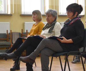 Grupa ludzi wewnątrz budynku siedzi na krzesłach, 