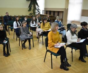 Grupa ludzi wewnątrz budynku siedzi na krzesłach, 