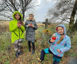 Uczennice trzymają zapalone znicze, które postawią na mogile