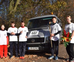 Parking. Pięć osób stoi przy samochodzie. Na samochodzie napis Bieg 
Pamięci

