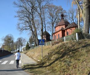 Droga. Biegnie jedna osoba. Po prawej stronie kościół