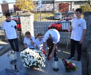 Cmentarz. Przy pomniku-mogile pięć osób. Zapalają znicz