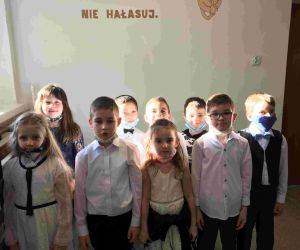 Uczniowie klasy I w strojach galowych i maskach, z przypiętymi kotylionami w barwach narodowych.