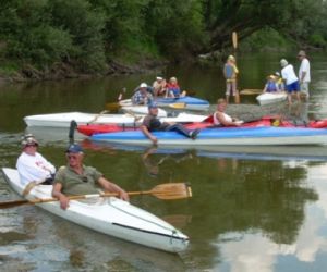Rzeka w otoczeniu drzew i krzewów, na rzece ludzie w kajakach