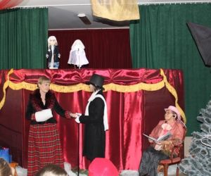 Kukiełki w przedstawieniu teatrzyku kukiełkowym. Osoby odgrywają scenkę teatralną przed parawanem.