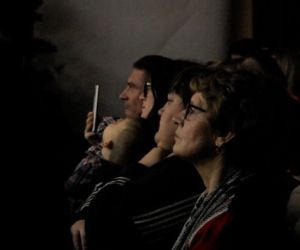 Osoby siedzą w zadumie, oglądając teatrzyk.