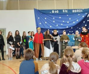 Uczniowie biorący udział w jasełkach stoją na tle świątecznych dekoracji